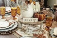 a cozy rustic Thanksgiving tablescape with an embroidered table runner and rust plaid napkins, a stand with faux pumpkins, leaves and pinecones