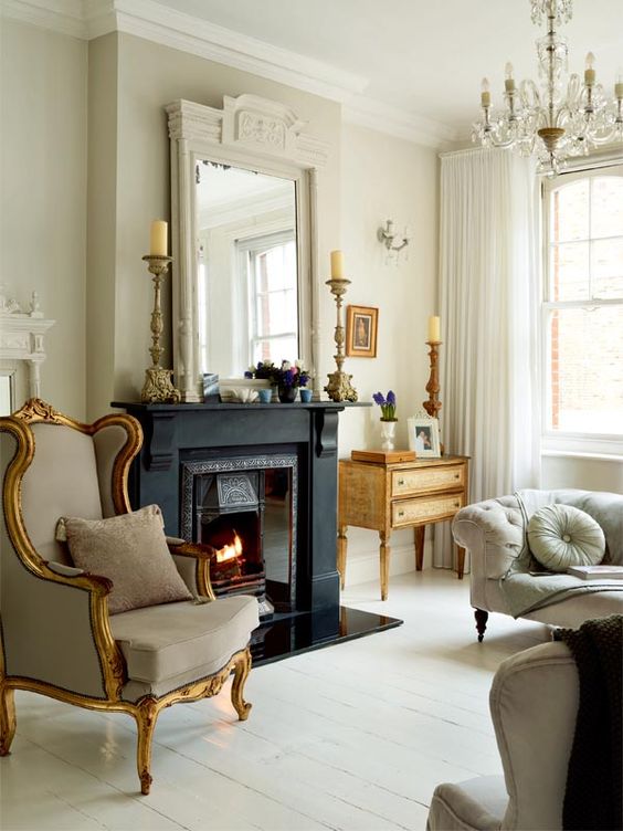 a creamy vintage living room with a fireplace clad with black, neutral vintage seating furniture, a vintage chandelier