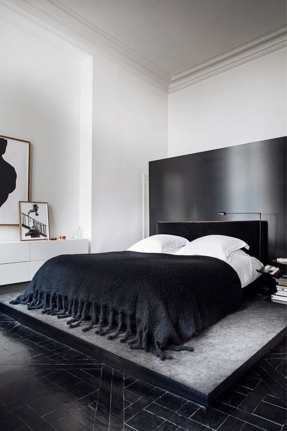 a dramatic black and white bedroom with a black accent wall, a black upholstered bed, black and white bedding, a white dresser and some art
