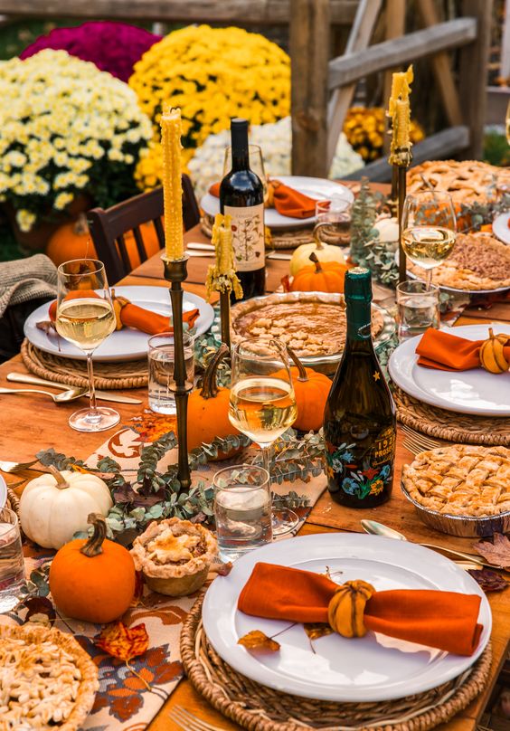 a fantastic Thanksgiving tablescape with orange napkins and pumpkins, mustard candles, woven placemats and greenery