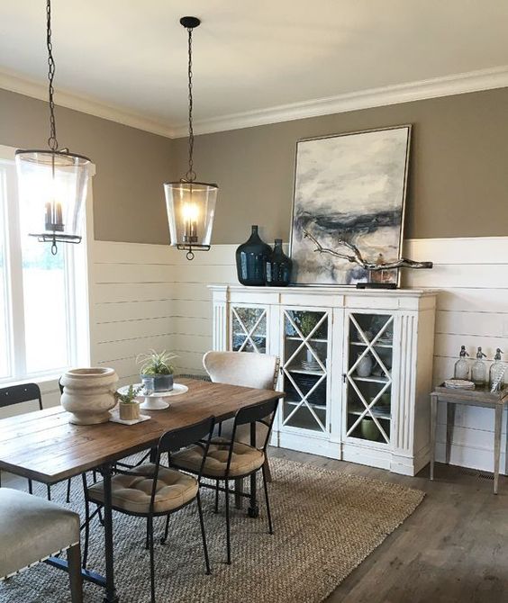 a farmhouse dining room with taupe walls and shiplap, a white glass cabinet, a stained table and upholstered chairs