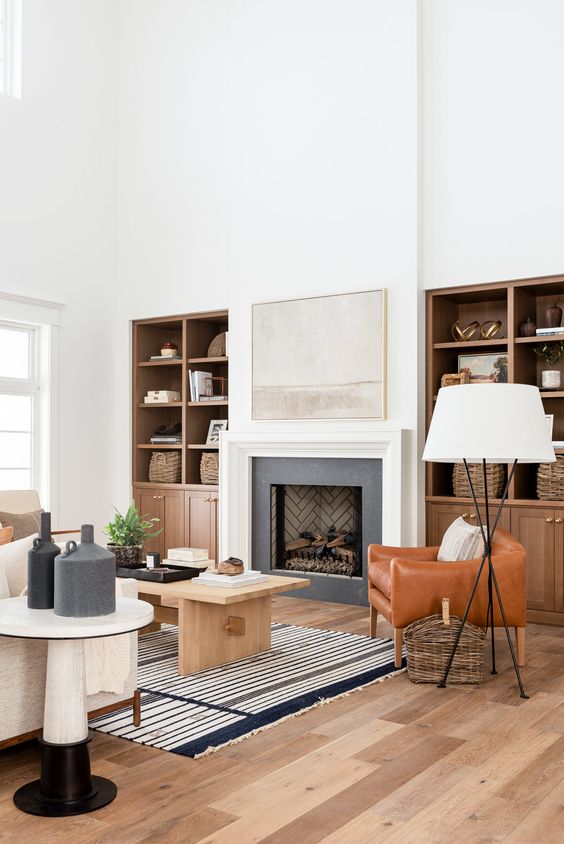 a farmhouse living room with a built-in fireplace and shelves, an amber leather chair, a wooden coffee table and neutral sofas