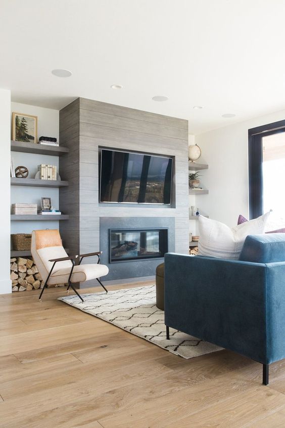 a farmhouse living room with a built-in fireplace, built-in shelves, a blue sofa, neutral chairs and a taupe stool