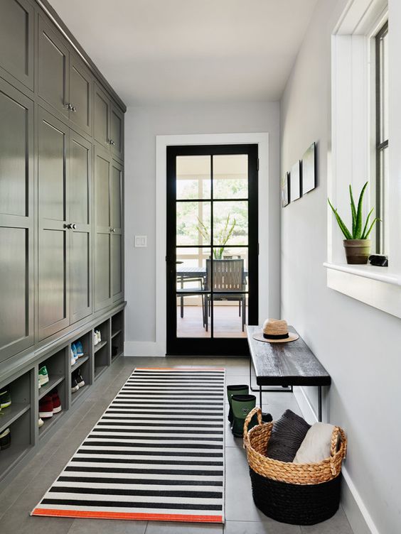 a farmhouse mudroom with a black storage unit, a striped rug, a black bench and a basket with pillows