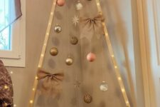 a frame Christmas tree lined up with lights, with gold, coral and silver ornaments hanging on threads plus some gold bows