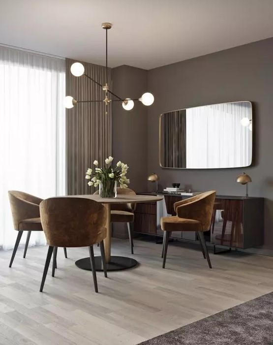 a glam and chic taupe dining room with a round table, rust colored chairs, a glossy floating credenza and a large mirror