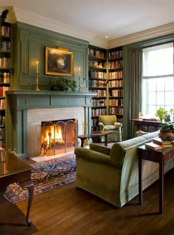 a green vintage living room with a fireplace with a metal screen, a green sofa and chairs, built in bookcases and some potted greenery