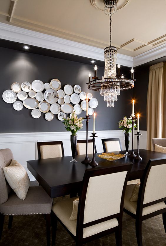 a jaw-dropping dining room with black walls, a black table, neutral chairs, a chic chandelier and a gallery wall of plates
