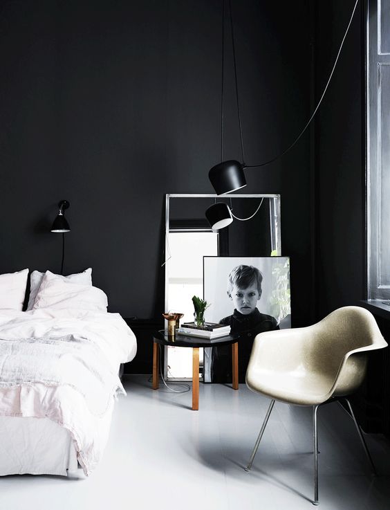 a laconic black and white bedroom with black walls, a bed with white bedding, a white leather chair and a mirror