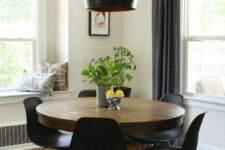 a mid-century modern dining nook with a round table, black chairs, a black pendant lamp, greenery and printed pillows