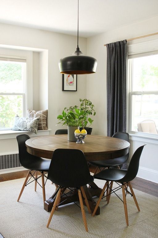 a mid century modern dining nook with a round table, black chairs, a black pendant lamp, greenery and printed pillows