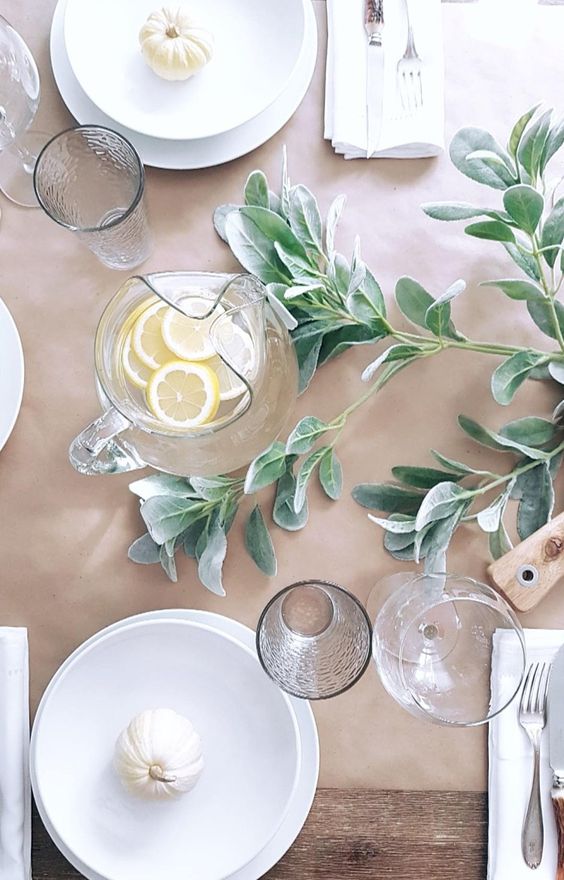 a minimalist Thanksgiving table with a kraft paper runner, greenery, white porcelain and clear glasses is amazing
