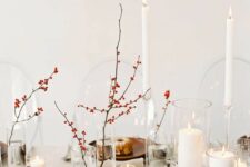 a minimalist Thanksgiving tablescape done in neutrals, with berries in vases, tall and thin and pillar candles, rust-colored plates and silver cutlery