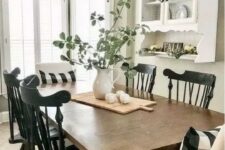 a modern farmhouse dining space done in black and white, with a stained table,a white wall-mounted shelf and black chairs, a vintage chandelier