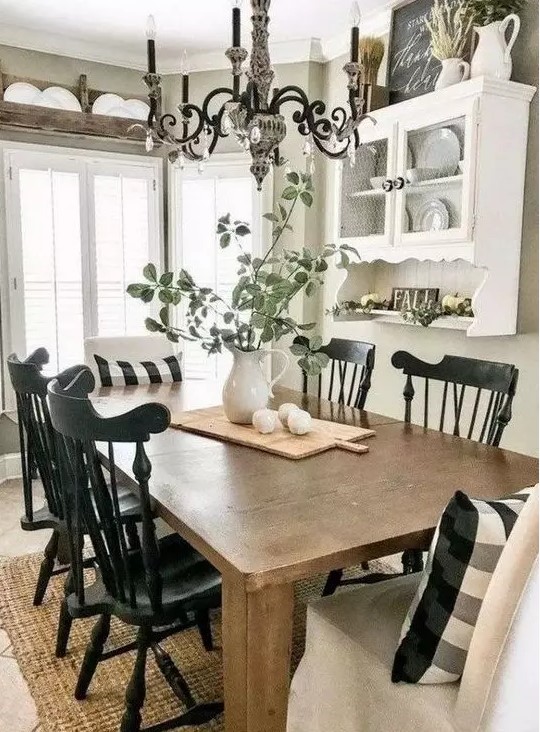 a modern farmhouse dining space done in black and white, with a stained table,a white wall-mounted shelf and black chairs, a vintage chandelier