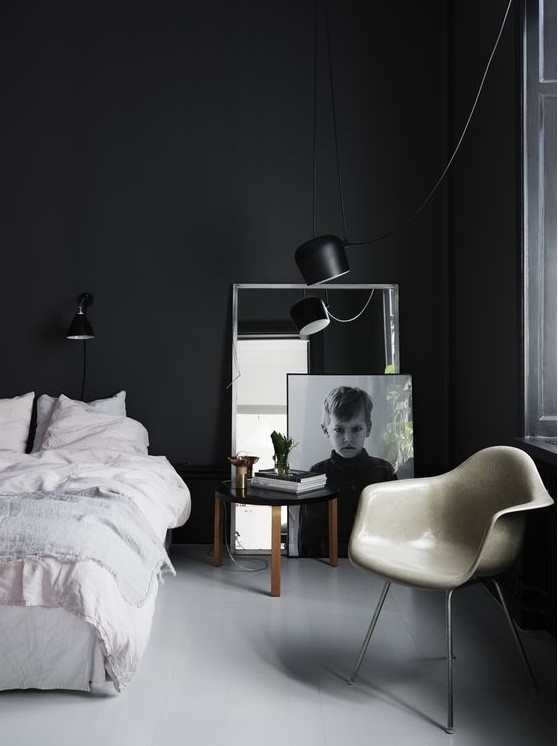 a moody Scandinavian bedroom with black walls, a white bed, a photo and a mirror plus a chair