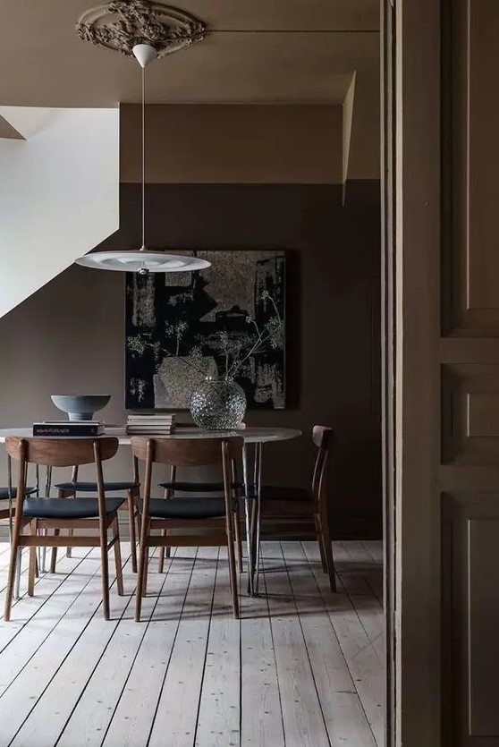 a moody all taupe dining space with a neutral floor, an oval hairpin leg table, black chairs and a pendant lamp