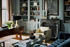 a moody vintage living room with pastel blue built-in bookcases, a fireplace with a black marble mantel, a navy sofa and vintage furniture