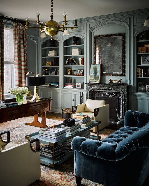 a moody vintage living room with pastel blue built in bookcases, a fireplace with a black marble mantel, a navy sofa and vintage furniture