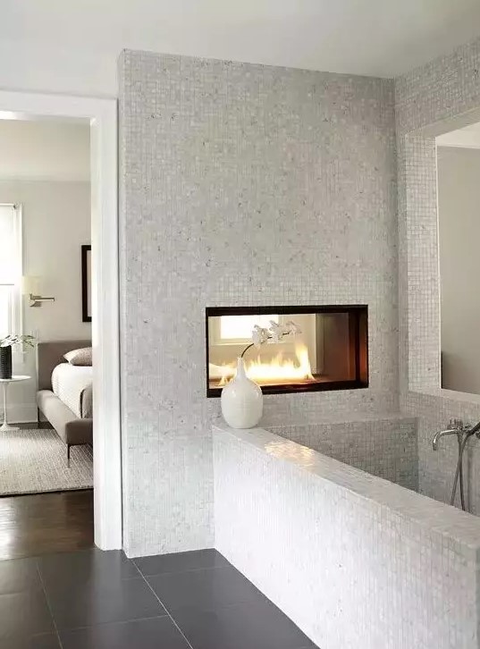 a neutral bathroom with small scale tiles, a double-sided fireplace, a bathtub clad with tiles is a chic idea to rock