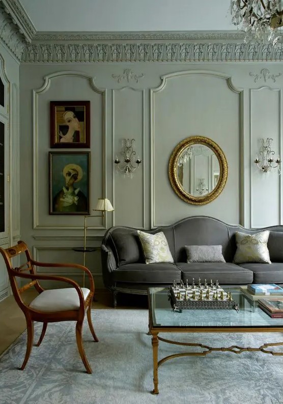 a neutral living room with elegant and refined paneling, a grey sofa, neutral chairs, a glass coffee table and some lovely artwork