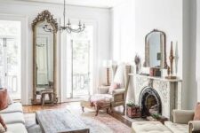 a neutral vintage living room with an ornate fireplace, neutral seating furniture, a low coffee table, a tall mirror in a fab frame and a chic chandelier