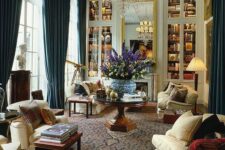 a neutral vintage living room with built-in bookcases, neutral sofas and chairs, a dark-stained coffee table and a fireplace wows