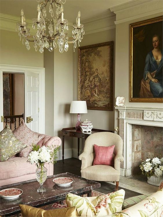 a neutral vintage living room with stone clad fireplace, vintage artworks, a pink and green sofa, a crystal chandelier