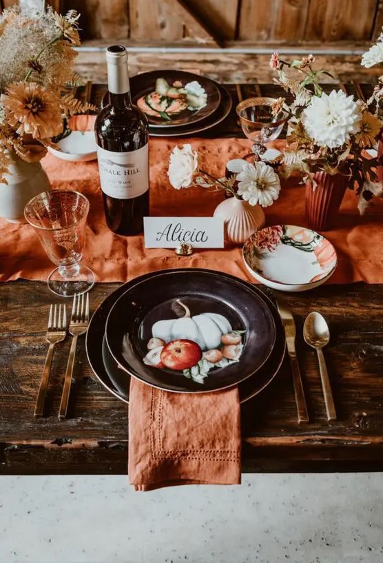 a pretty rust colored Thanksgiving tablescape with rust linens and vases, dried and fresh blooms, painted black plates