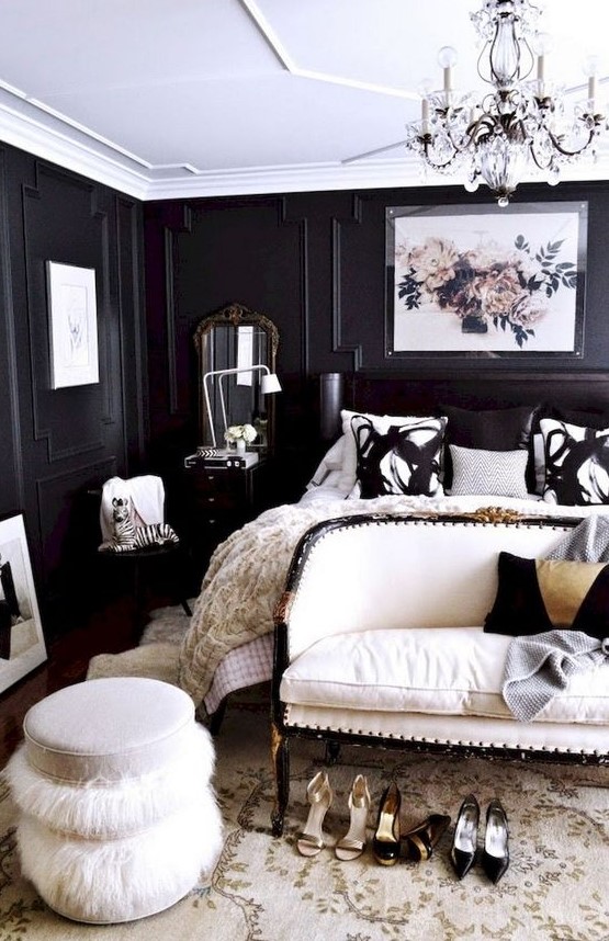 a refined and luxurious black and white bedroom with paneled walls, a black bed, a white upholstered loveseat and a fluffy ottoman