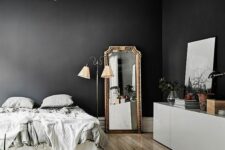 a refined black and white bedroom with black walls, molding, a bed with grey bedding, a white cabinet and a floor mirror