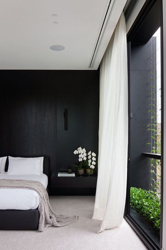 a refined minimalist black and white bedroom with a statement wall, a black bed, white curtains and stylish bedding