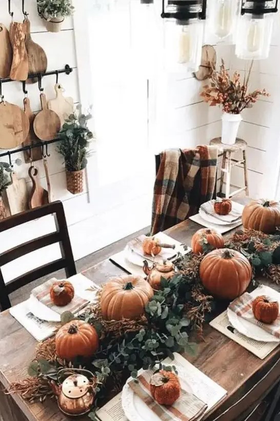 a simple rustic Thanksgiving table with a lush greenery runner, rust pumpkins and gourds, copper teapots and mugs