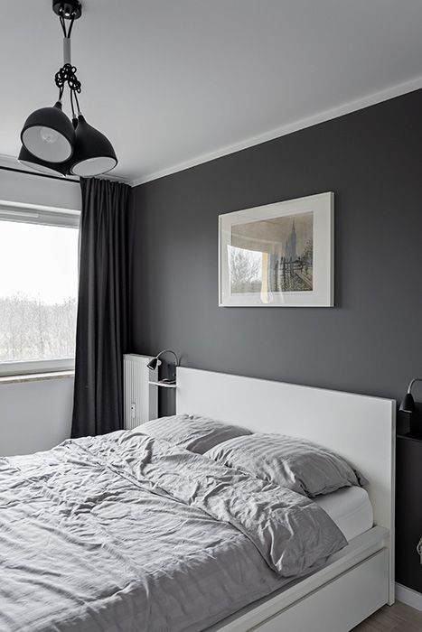 a small and cool Scandinavian bedroom with a black accent wlal, a white bed and grey bedding, black pendant lamps