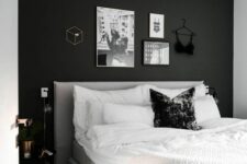 a small and cozy bedroom with a black accent wall, a grey bed with neutral bedding, a black nightstand and a gallery wall