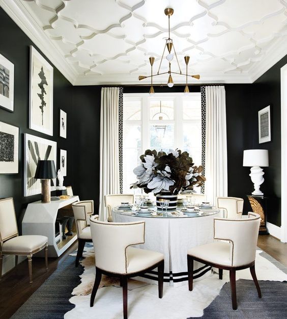 a sophisticated black and white dining room with black walls and a white ceiling, a round white table and catchy chairs, a lovely console table and gilded touches