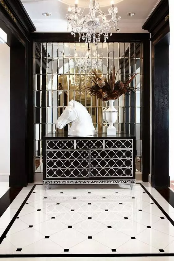 a sophisticated black and white foyer with a mirror wall, a black and white inlay dresser, black and white tiles, a horse bust and a crystal chandelier