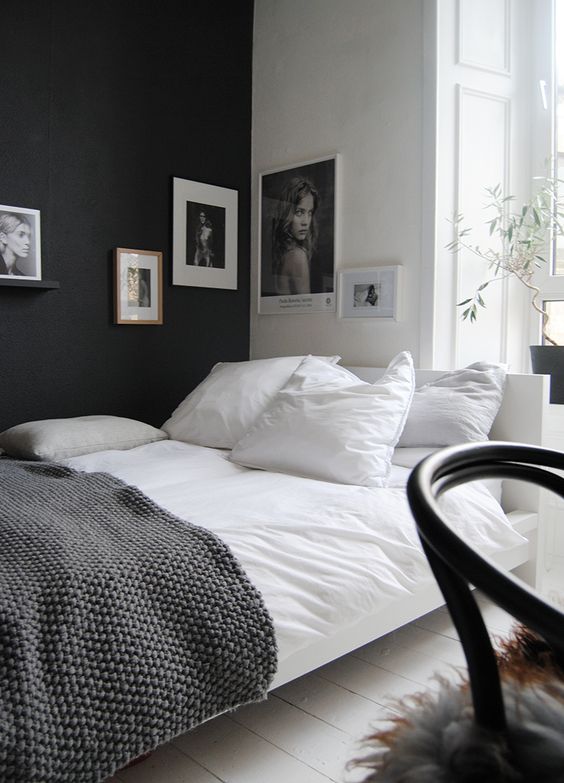 a stylish Scandinavian bedroom with a black accent wall, a bed with monochromatic bedding, a corner gallery wall