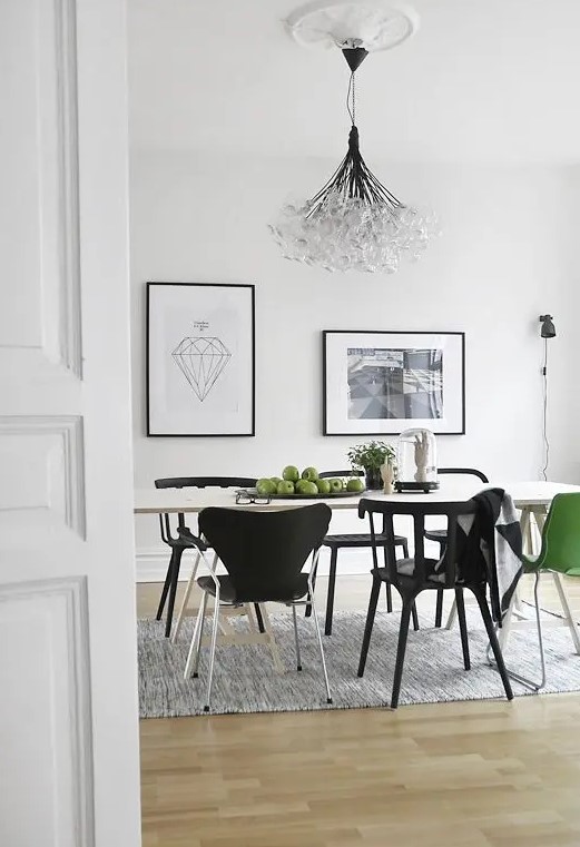 a stylish Scandinavian dining room with a white table, black chairs and a green one for an accent, a small gallery wall and a bubble chandelier