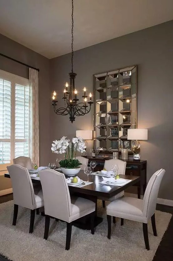 a stylish and exquisite taupe dining room with a dark stained table and a credenza, neutral chairs, a black vintage chandelier and a mirror piece on the wall