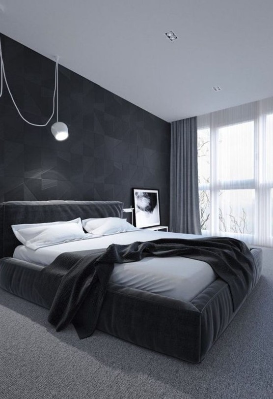 a stylish minimalist bedroom with a geometric accent wall, an upholstered black bed and a white pendant lamp