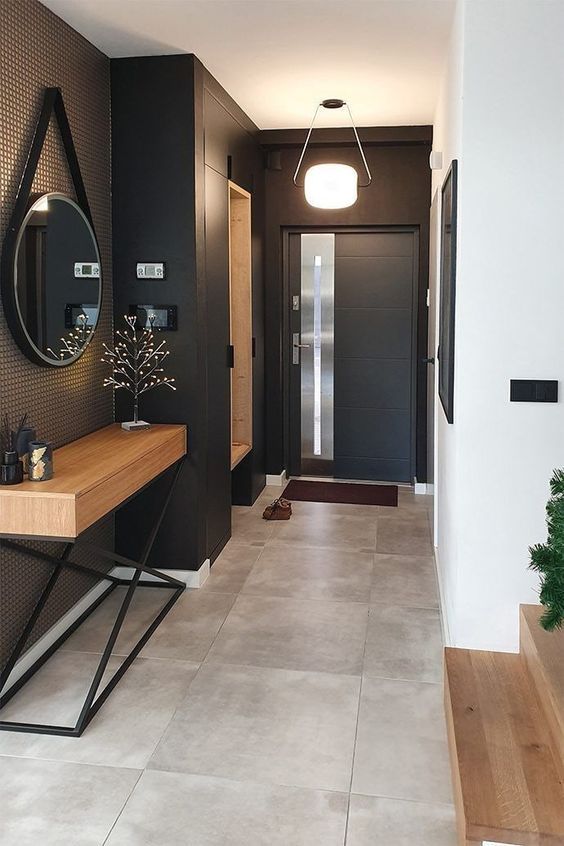 a stylish modern entryway with black walls and a door, a built-in storage unit, a stained console table and a round mirror