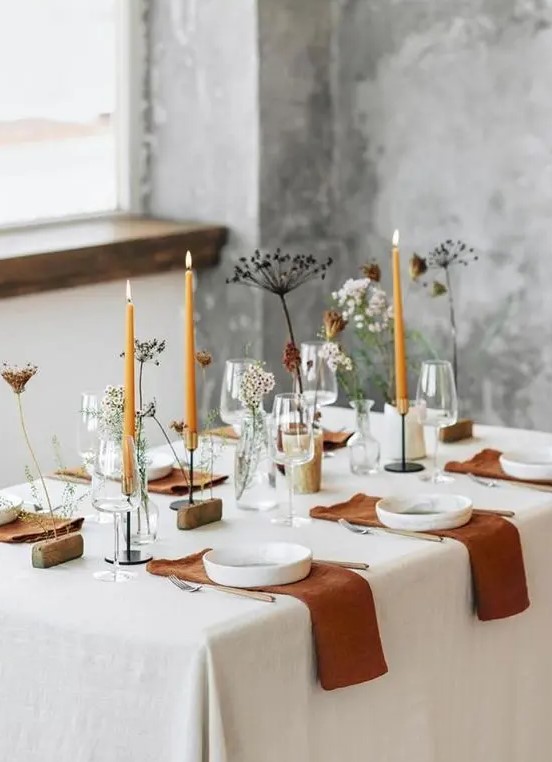 a stylish modern meets boho Thanksgiving tablescape with rust napkins and candles, fresh and dried blooms, white plates and wooden stands