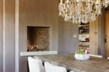 a taupe dining room with a built-in fireplace, a wabi-sabi wooden table, white upholstered chairs, crystal chandeliers