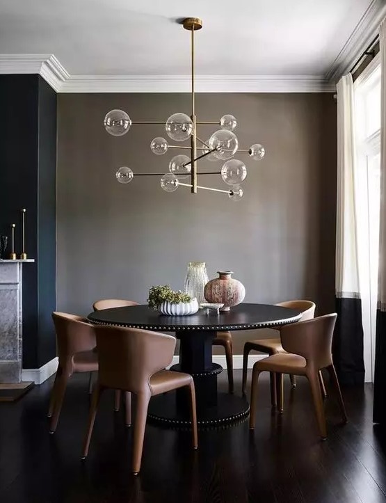 a taupe dining space wiht a large round table in black, rust colored leather chairs and a catchy bubble chandelier