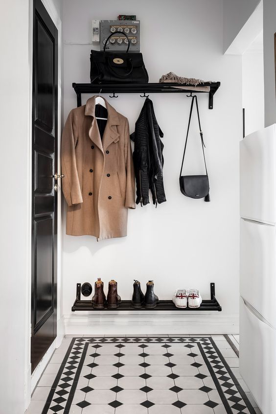 a tiny and cool black and white entryway with a wall mounted shoe shelf, a rack and black and white tiles on the floor