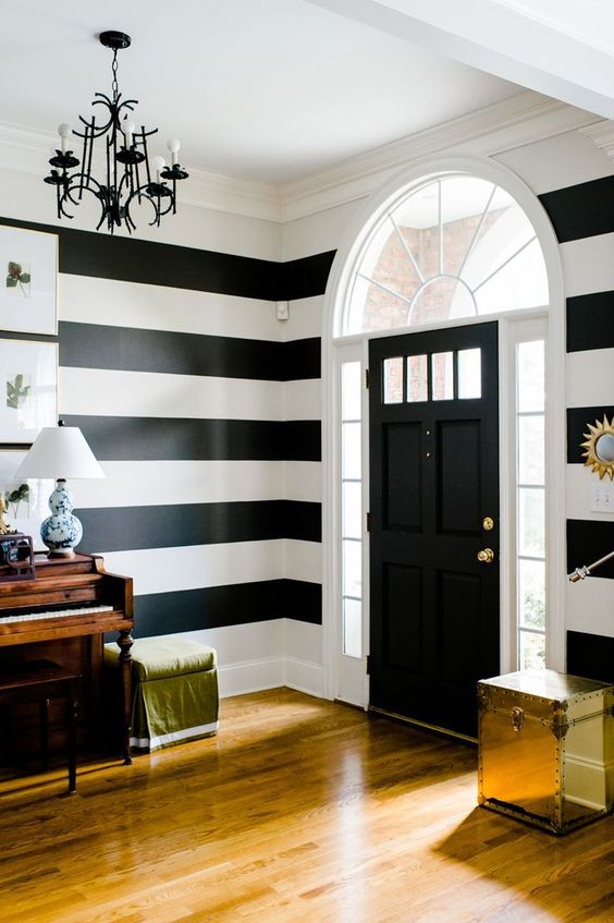 a vintage foyer with a striped wall, a glossy chest, a stool and a vintage piano is a lovely and cool space