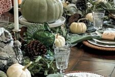 a vintage green thanksgiving tablescape with a green table runner and napkins, green pumpkins and eucalyptus, candles and pinecones