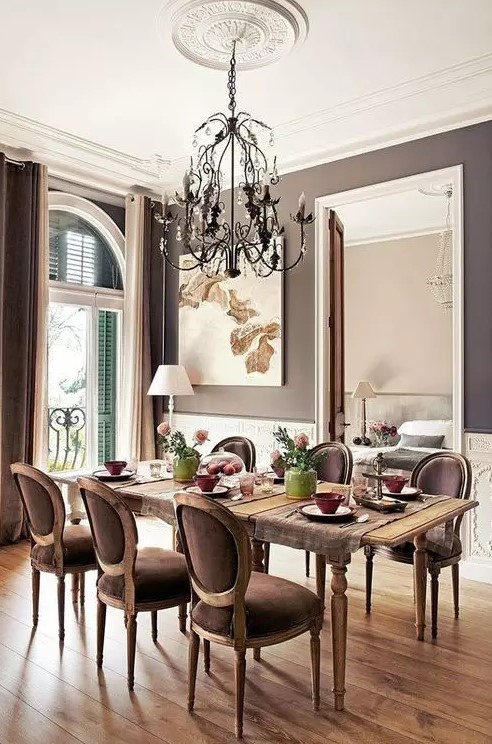 a vintage inspired taupe dining zone with creamy paneling, a vintage table and taupe chairs, a chic chandelier and some art plus shutters on the window