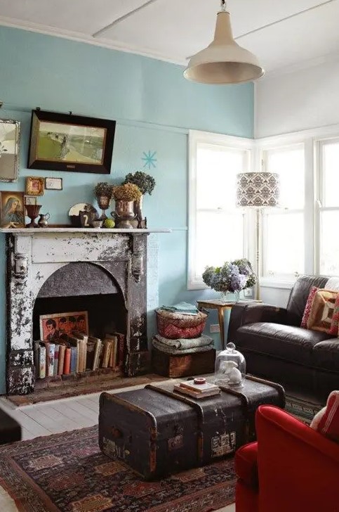 a vintage meets eclectic living room with a blue accent wall, a non-working fireplace used for book storage, a gallery wlal and a pendant lamp plus a chest as a coffee table